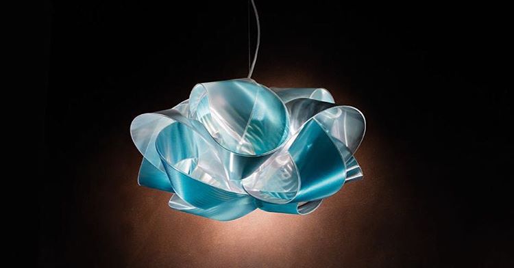 Fabula is a softer soul, an intertwining of the elements of water and air that render its enveloping design mysterious and suggestive. It is made by hand, using interlinking pieces of Lentiflex®, which in reflecting the internal light source, give it the look of a long and soft silk ribbon. The coloured models have a transparent layer and a printed layer obtained by using a morphing technique, that together, create a tenuous and delightful shade of aquamarine or honey.